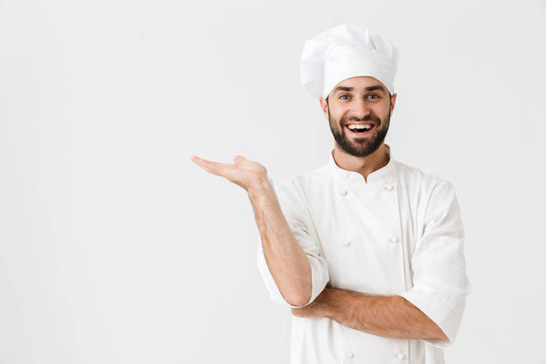 Happy young chef posing isolated over white wall background in uniform showing copyspace. - Foto, imagen