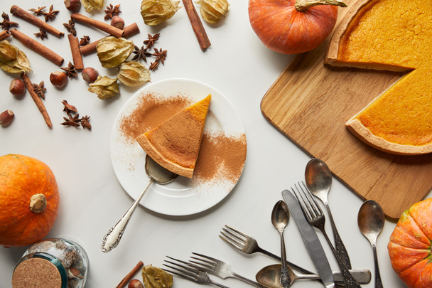 top view of tasty pumpkin pie near whole pumpkins, cutlery and spices on white marble surface - 写真・画像