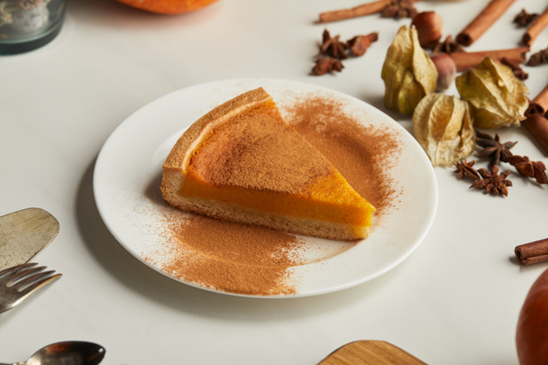 tasty pumpkin pie with cinnamon powder near cutlery and spices on white marble surface - Photo, Image