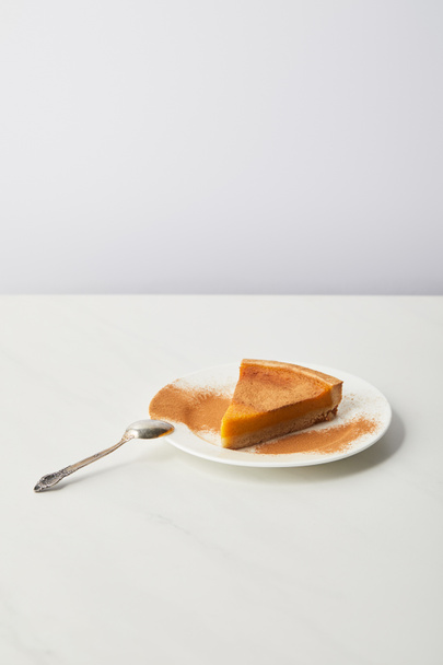 delicious pumpkin pie with cinnamon powder on plate near spoon of white marble table isolated on grey - Foto, immagini