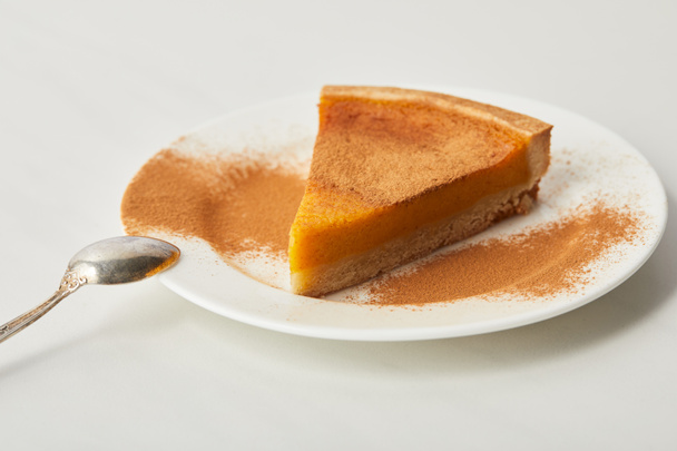 tasty pumpkin pie with cinnamon powder on plate near spoon of white marble table - Foto, afbeelding