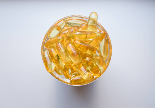 Fish oil capsules on a glass plate. A lot of vitamin omega 3 on a white background. Close-up, top view, high resolution product. Metabolism in the body. The body of calcium. A quick way to lose weight - Fotó, kép