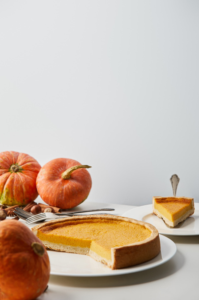 white plates with delicious pumpkin pie near whole pumpkins, cutlery and spices isolated on grey with copy space - Foto, imagen