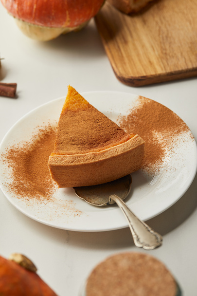 selective focus of delicious pumpkin pie with cinnamon powder on plate with spatula on white marble table - Foto, Bild
