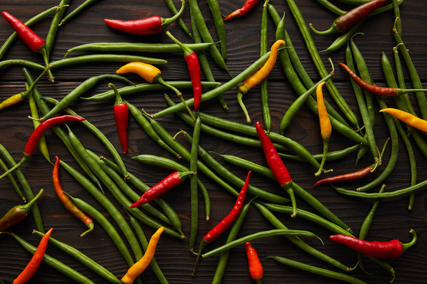 top view of chili peppers and green peas on wooden table  - Фото, изображение
