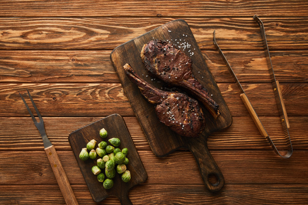 top view of meat and brussels sprouts on cutting boards with grill tools  - Fotoğraf, Görsel
