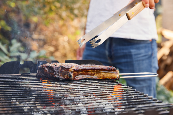 cropped view of man with tweezers grilling meat on barbecue grid  - Foto, immagini
