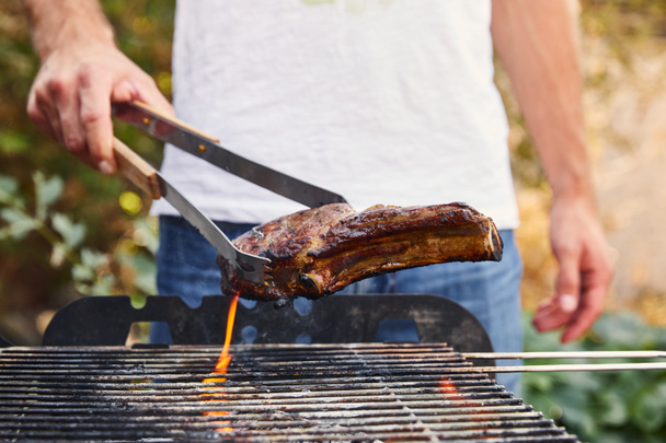 cropped view of man with tweezers grilling meat on barbecue grid  - Photo, Image