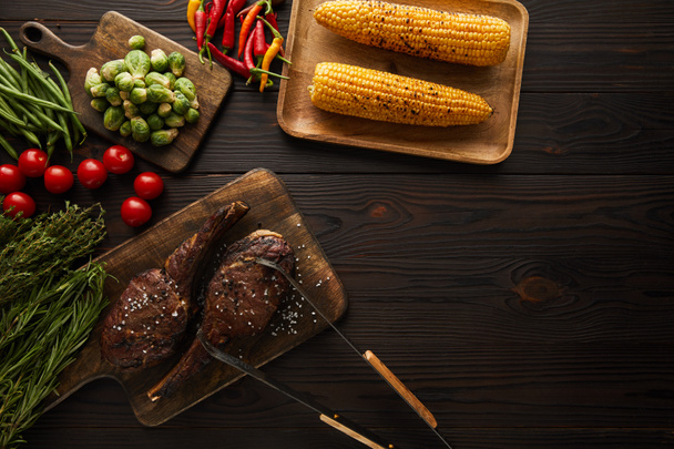 vista superior de la carne, maíz, chiles, tomates cherry, guisantes verdes, vegetación, coles de Bruselas en la tabla de cortar, pinzas
 - Foto, imagen