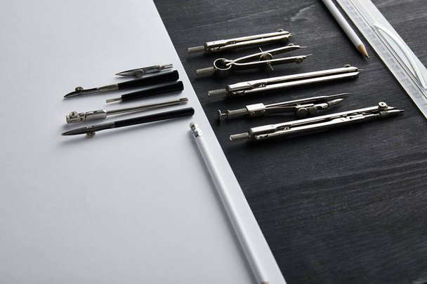 bílý papír s kopírovacím prostorem a kompasy, pravítko, tužky na černém a dřevěném stole  - Fotografie, Obrázek