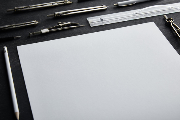 weißes Papier mit Kopierraum und Zirkel, Lineal, Bleistift, Stift auf schwarzem und hölzernem Tisch  - Foto, Bild
