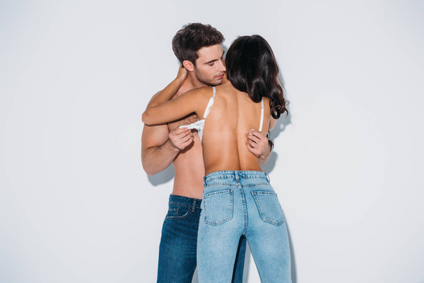 handsome man taking off bra from girl in blue jeans on grey background - 写真・画像