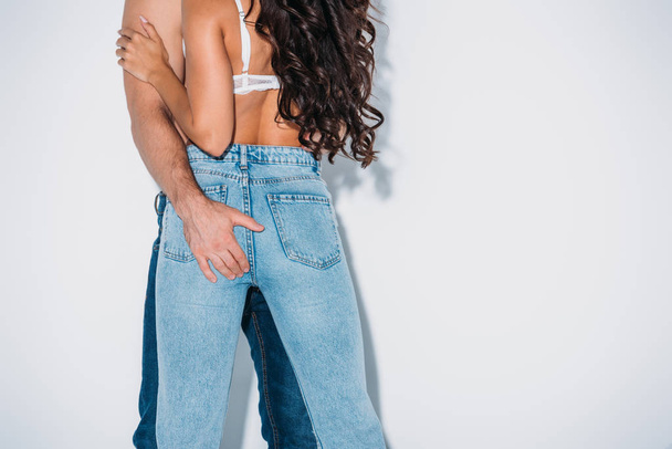 cropped view of man touching buttocks of girl in blue jeans on grey background - Photo, Image