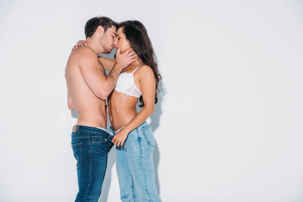 young man kissing girl unbuttoning his jeans on grey background - Photo, Image