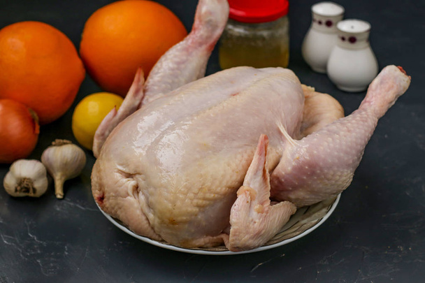 Pollo crudo si prepara per la cottura in forno con miele, arance, limoni e aglio, fondo scuro, orientamento orizzontale
 - Foto, immagini
