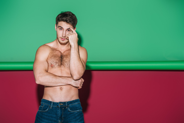 sexy shirtles man in denim jeans looking at camera on green and red background - 写真・画像