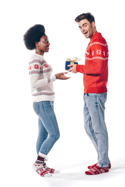 smiling interracial couple in winter sweaters holding christmas present, isolated on white - Photo, Image