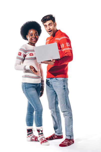 шокована мультикультурна пара в светрах з ноутбуком, ізольована на білому
  - Фото, зображення