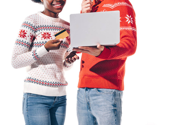 vista recortada de pareja interracial sosteniendo el uso de ordenador portátil con tarjeta de crédito, aislado en blanco
  - Foto, imagen