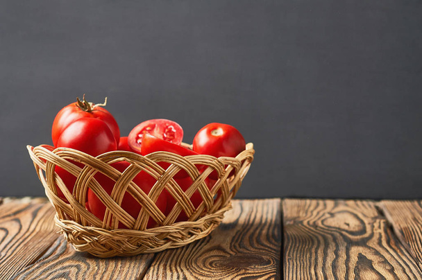 Full wicker basket of tomatoes lies on old rustic wooden table. Space for text - Photo, image