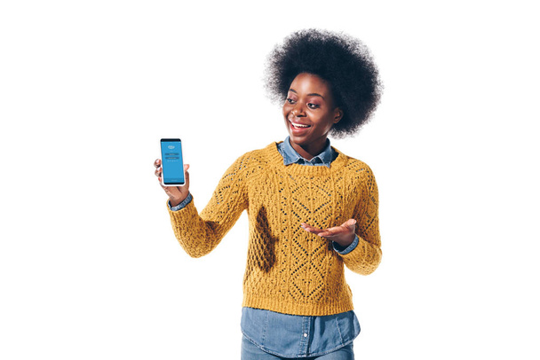 KYIV, UKRAINE - AUGUST 21, 2019: african american girl showing smartphone with skype app on screen, isolated on white - Φωτογραφία, εικόνα