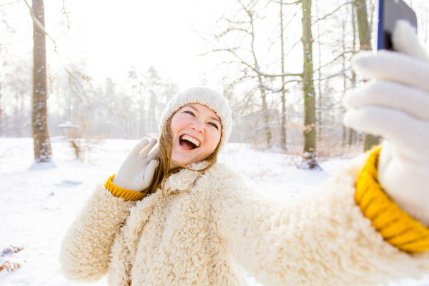 beautiful happy young woman taking selfie with smartphone in winter forest - Foto, Bild