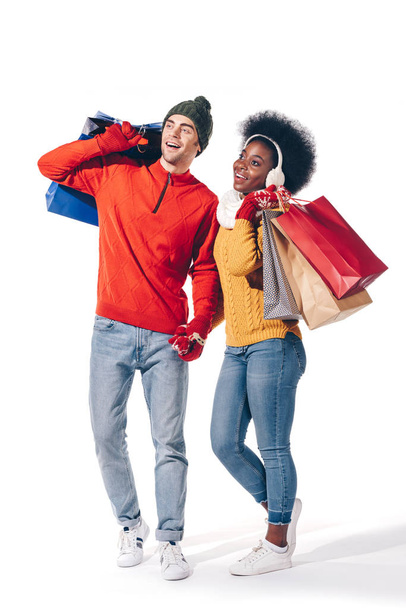 interracial couple in winter sweaters holding shopping bags, isolated on white - Zdjęcie, obraz