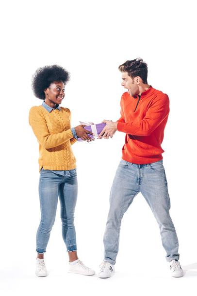 shocked boyfriend and smiling african american girlfriend holding gift box, isolated on white  - Φωτογραφία, εικόνα