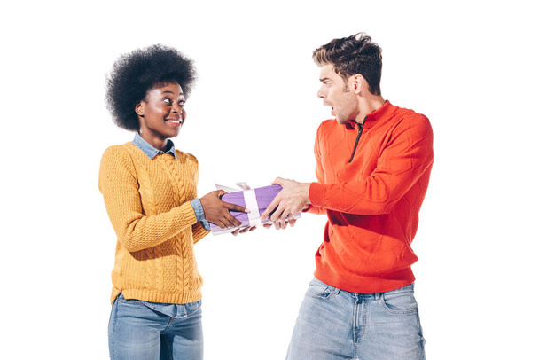 geschokte man en glimlachend Afrikaans amerikaans meisje houden geschenk, geïsoleerd op wit  - Foto, afbeelding