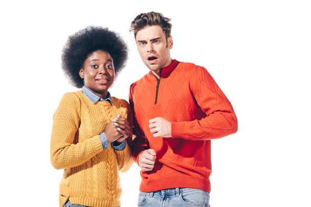 shocked multicultural couple in yellow and red sweaters, isolated on white  - Фото, изображение