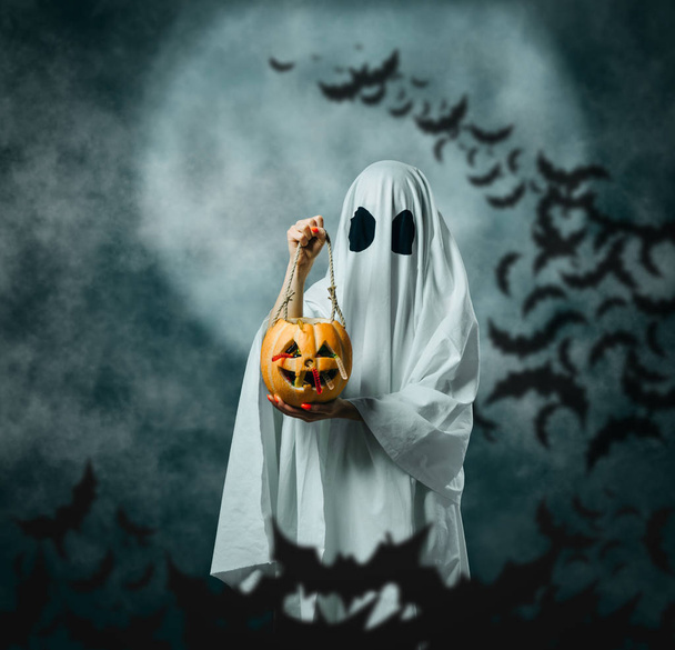 Fantasma blanco sosteniendo una calabaza tallada con caramelos en Halloween n
 - Foto, Imagen