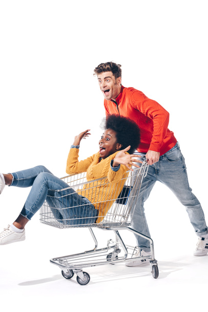 multiethnic couple having fun with shopping cart, isolated on white - Φωτογραφία, εικόνα