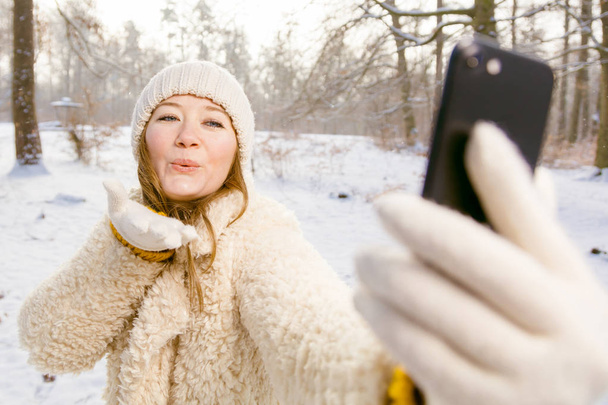 beautiful smiling young woman taking selfie with smartphone in winter forest - Foto, Bild