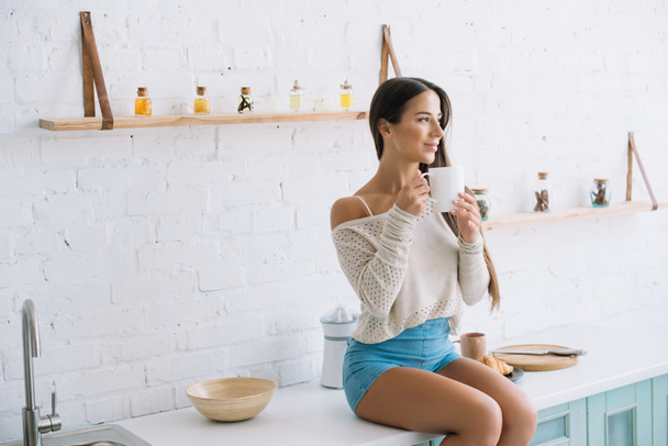 happy young woman holding cup of coffee in kitchen - Foto, Imagem