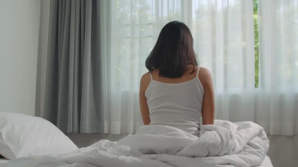 Tiener Spaanse vrouw wordt thuis wakker. Jong Aziatisch meisje stretching na wakker beginnen van een nieuwe dag met energie en vitaliteit op bed in de buurt van raam in de slaapkamer 's morgens, achteraanzicht. Slow motion shot. - Video
