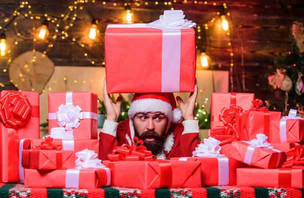 Best prices for winter gifts. Man Santa hat peeking out of pile of gifts. Bearded Santa Claus and many holiday packages. Santa with gifts. Seasonal offer. Christmas sale. Holidays filled with fun - Фото, зображення