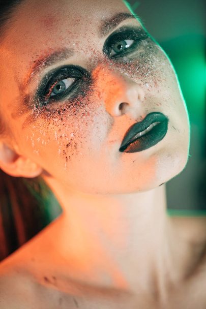 ein atemberaubendes Make-up auf dem Gesicht eines schönen jungen Mädchens, Schönheits-Make-up, Öl auf ihrem Gesicht und glitzerndes Grün mit Priorität Rot - Foto, Bild