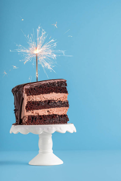 Chocolate cake slice with sparkler. Birthday cake on blue backgr - Φωτογραφία, εικόνα