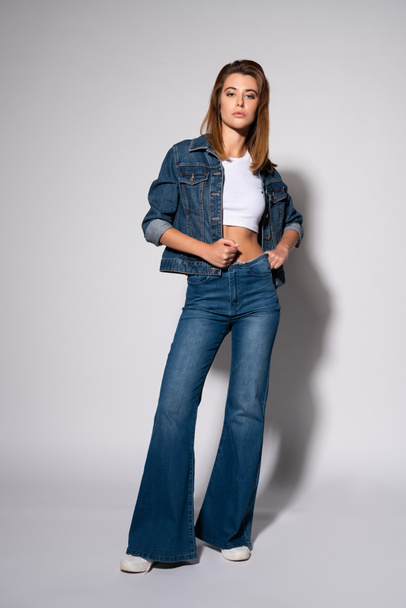 stylish girl touching jeans while standing on white  - Фото, зображення