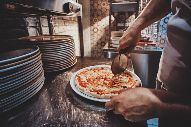 Chef-kok is snijden vers bereide pizza - Foto, afbeelding