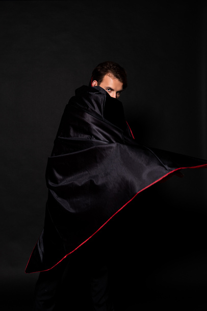 uomo che copre il viso con mantello di costume di Halloween su nero
  - Foto, immagini