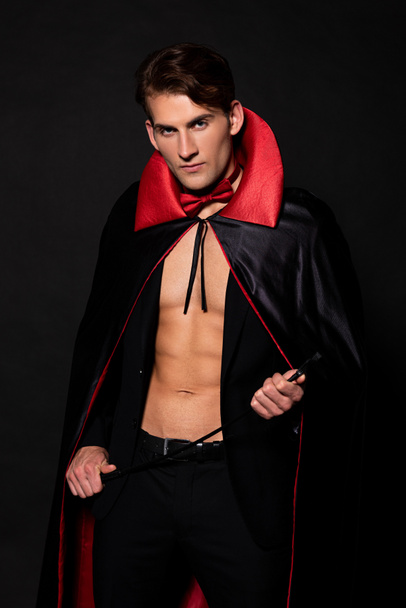 man in vampier halloween kostuum houden zweep geïsoleerd op zwart  - Foto, afbeelding