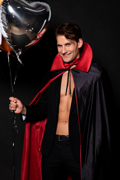 homme gai en costume vampire halloween tenant des ballons isolés sur noir
  - Photo, image