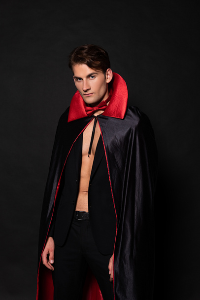handsome man in vampire halloween costume looking at camera isolated on black  - Zdjęcie, obraz