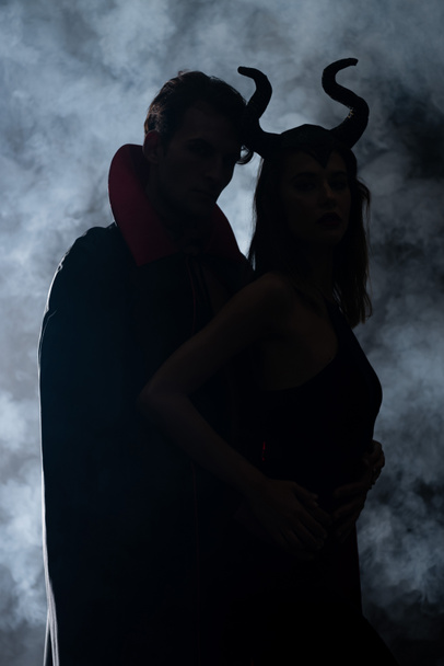 silhouette of man and woman in halloween costumes on black with smoke  - Foto, imagen