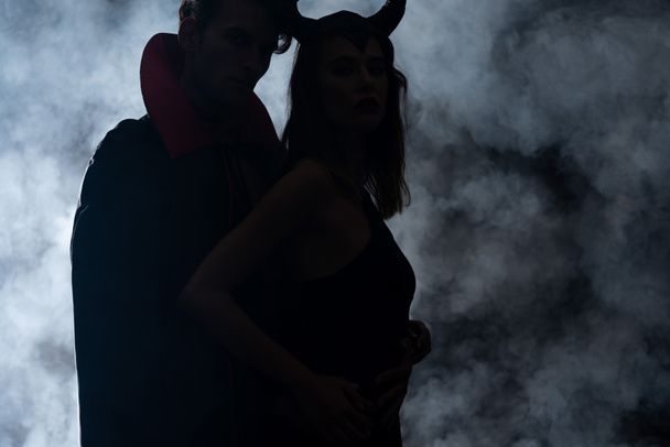 silhouet van man en vrouw in halloween kostuums staan op zwart met rook  - Foto, afbeelding