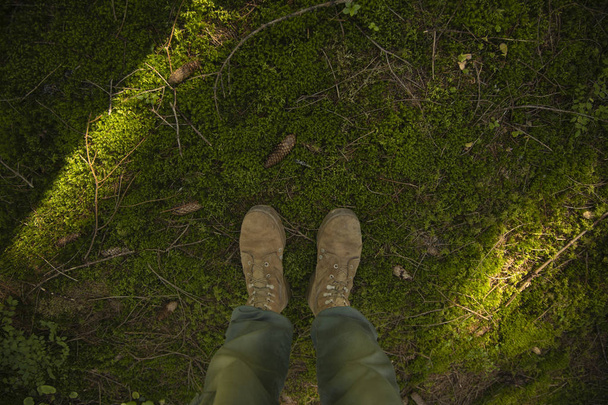 στρατιωτική ταξίδια και πεζοπορία φωτογραφία των αρσενικών ποδιών σε στρατιωτικές μπότες από πάνω σε δάσος πράσινο βρύα εδάφους  - Φωτογραφία, εικόνα