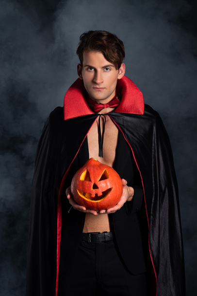 handsome man holding halloween pumpkin on black with smoke  - Photo, Image