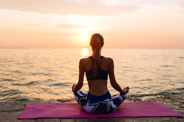 slank meisje oefenen yoga, zitten op pier, door de zee - Foto, afbeelding