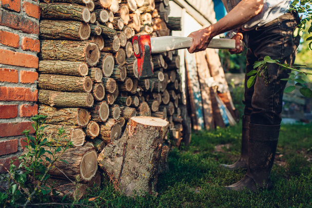 Робота з сокирою. Старший чоловік подрібнює дрова сокирою на сільському подвір'ї
. - Фото, зображення